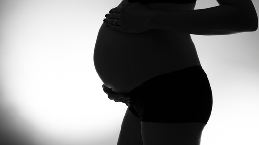 black and white image of a pregnant belly with a women holding it.