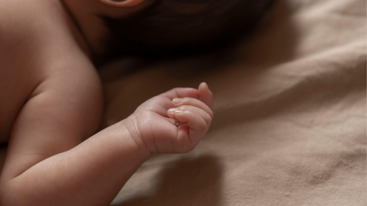 baby laying down with their hand curled on a bed/sheet
