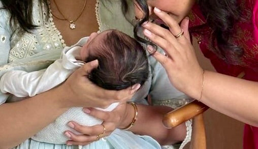 mom holding a baby while another women whispers intzo the baby's ear.