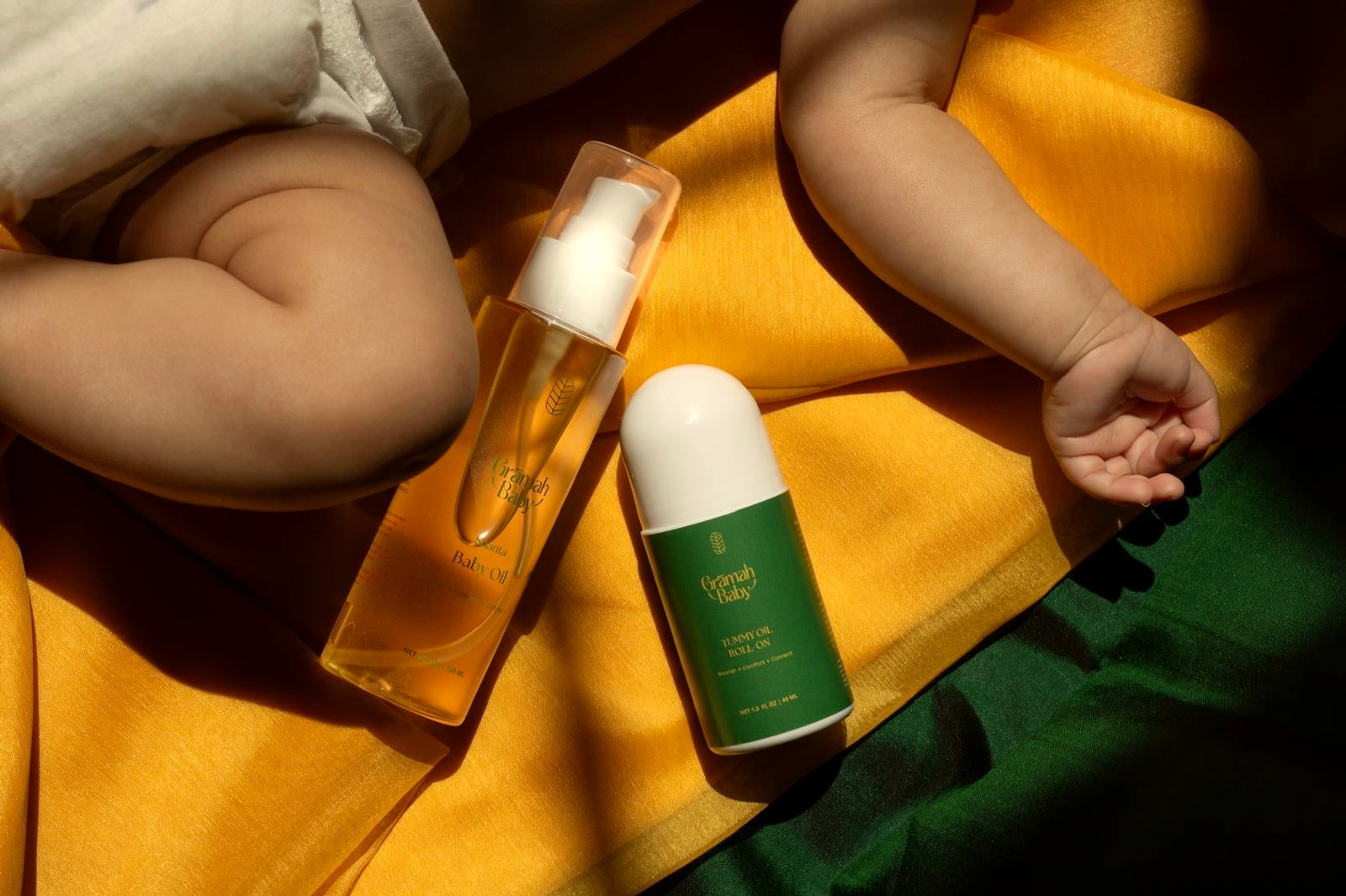 Two skincare products on a yellow surface with a baby's arm in the background