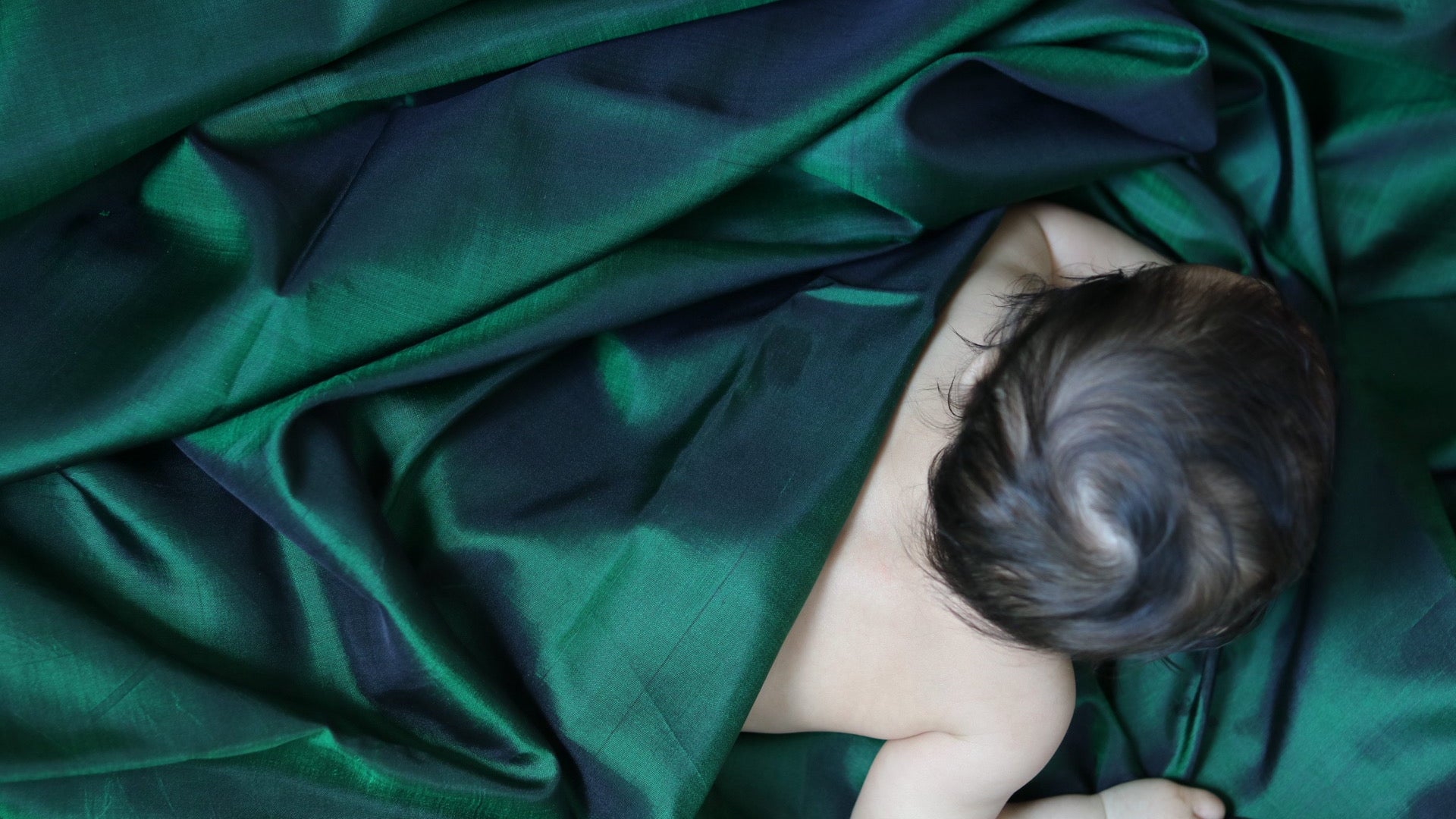 Baby lying under a green blanket