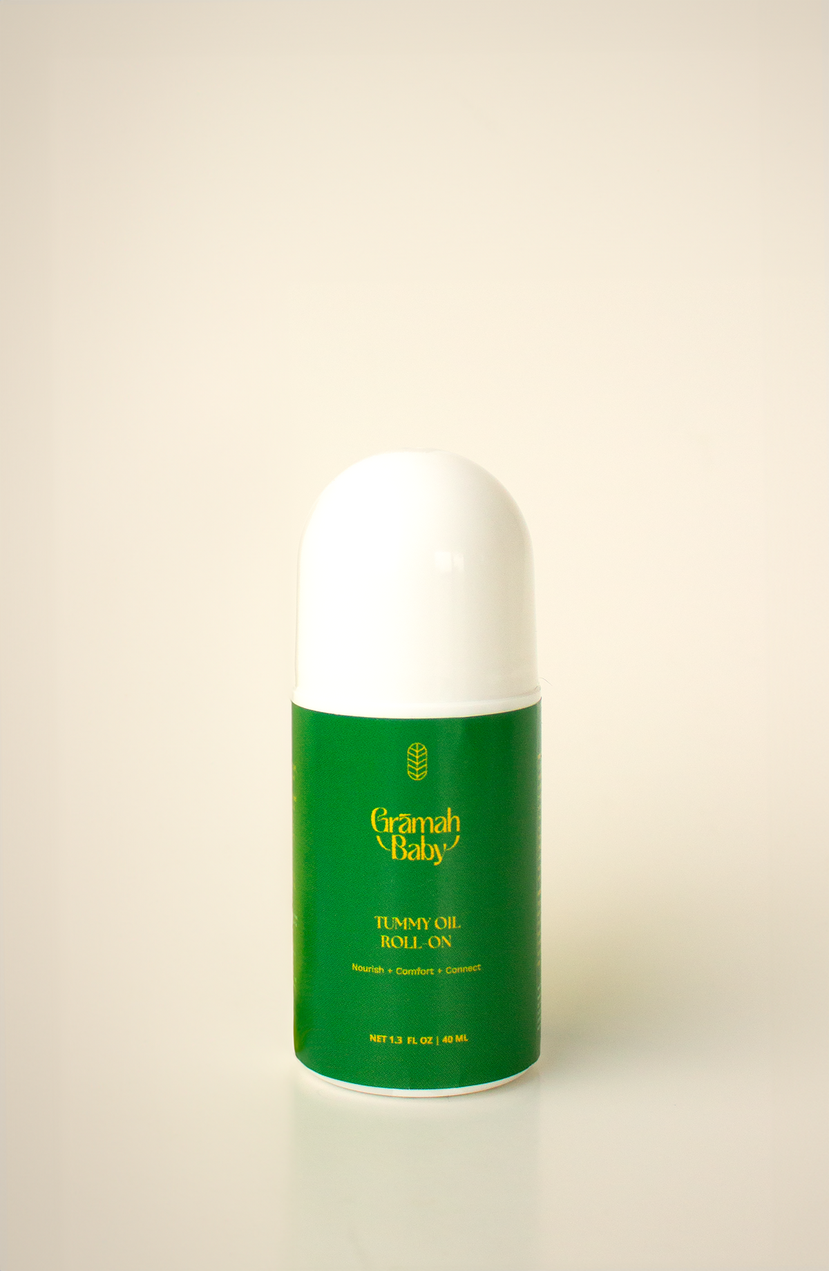 Grāmah Baby Tummy Oil Roll On with the cap on against an ivory background. The label is green with yellow lettering